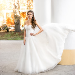 brunette bride in long white dress posing at windy day at park