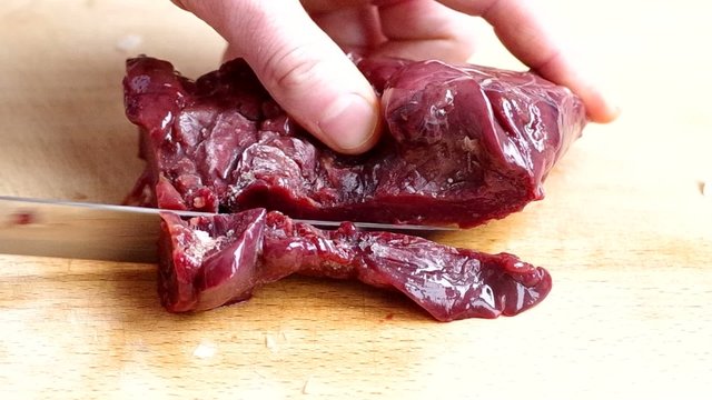 Slicing frozen chicken liver on wooden board