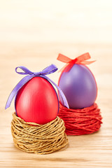 Painted Easter Eggs with bow in nests on wooden background
