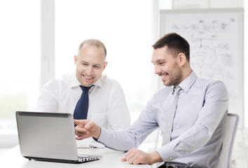 Fototapeta na wymiar two smiling businessmen with laptop in office