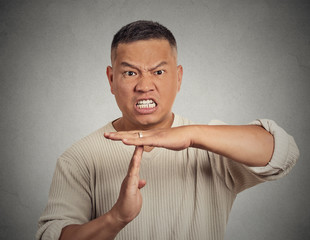 Angry man showing time out gesture on grey wall background 