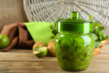 Tasty kiwi jam in glass jar on wooden background