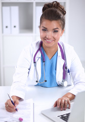 Female doctor sitting on the desk and working a laptop in