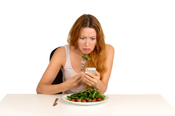 Displeased girl eating salad looking at mobile phone