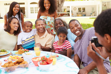 Multi Generation Family Enjoying Meal In Garden Together