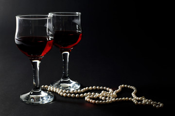Beautiful Pearl Necklace and Glass Cups of Red Wine on Black