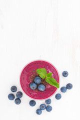 blueberry milkshake in a glass on white wooden table, vertical