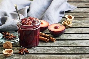 Homemade plum jam with walnuts and spices on a wooden table