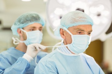 Young surgeon tying older surgeons mask