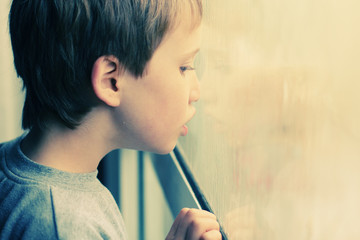 Cute 6 years old boy looking through the window