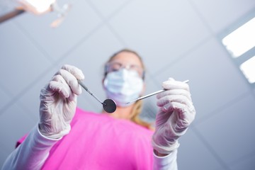 Dentist in surgical mask holding tools over patient