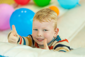Obraz premium A little boy lying on the floor surrounded by colorful balloons