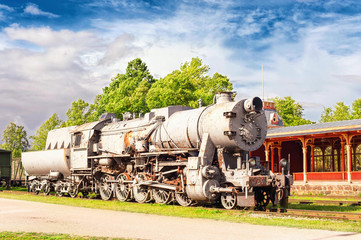 Fototapeta na wymiar Old rustic steam locomotive on station platform. Cloudy sky back
