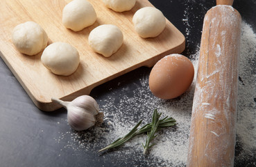 Garlic, rosmary, egg, rolling pin and pieces of dough on the woo