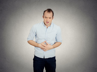man, doubling over in acute body stomach pain grey background 