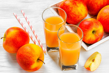 Glass of apple juice with apples on white wood background