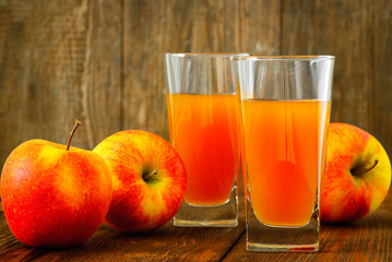 Two glasses of apple juice and apples on wooden background