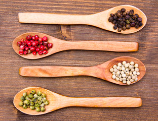 Wooden spoons with mixed peppers on wood seen from above