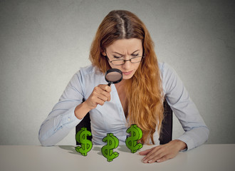 Businesswoman looking through magnifying glass at dollar signs