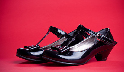 Black shine leather girl shoes with black ribbon isolated on red