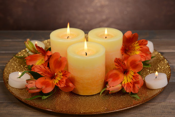 Obraz na płótnie Canvas Beautiful candles with flowers on table on brown background
