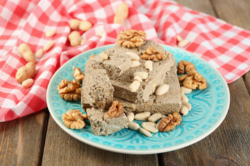 Sunflower halva with nuts on plate, on wooden background