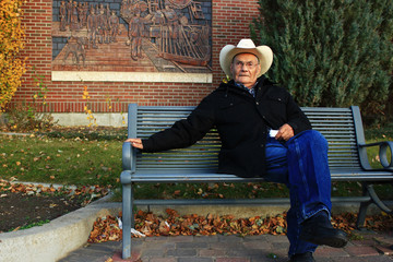 Old Man Wearing a Cowboy Hat sitting on a Park Bench