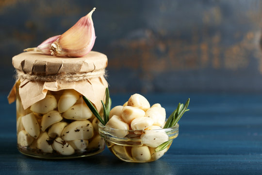 Canned garlic in glass jar on color wooden background