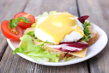 Toast with egg Benedict and tomato on plate on wooden table