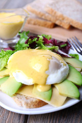 Toast with egg Benedict and avocado on plate on wooden table