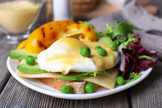 Toast with egg Benedict and avocado on plate on wooden table
