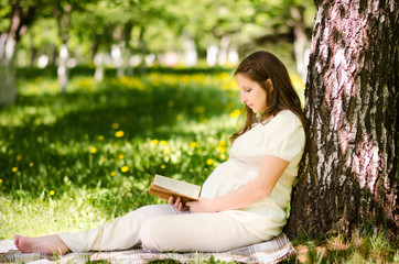 Beautiful pregnant woman in the park with book