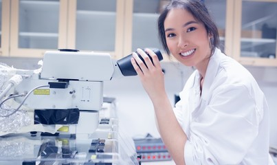 Pretty scientist smiling at the camera using microscope