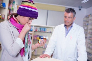 Obraz premium Sick girl with scarf and colorful hat holding a bottle of drug