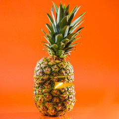 Artistic sliced, standing pineapple on orange background, square