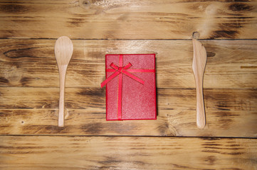 Red gift and spoon on wooden background.
