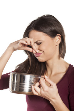 disgusted woman holding a pot with food and pinching her nose