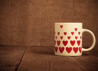 Mug with many pictured hearts on the old wooden table. Toned