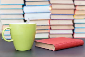 green cup next to the red book on a background of books