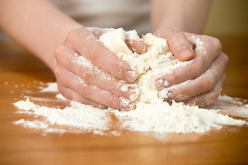 Woman’s hands knead dough on the table