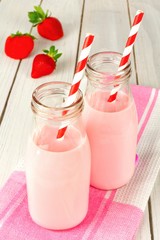 Strawberry milk in traditional bottles with straws on white wood
