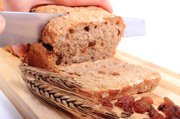Slicing fresh bread, ears of wheat and raisins