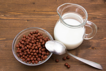 Bowl with chocolate cereals and milk jug on wood from above