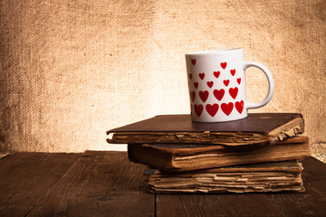 Old books and mug with many pictured hearts on the old wooden ta
