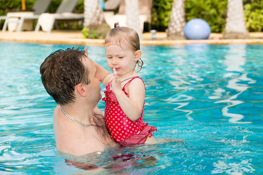 Active father teaching his toddler daughter to swim in pool