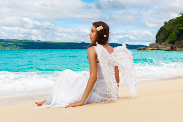 Fototapeta na wymiar Beautiful young bride with angel wings on the sea coast. Tropica