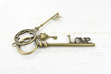 Love Three brass keys on a white distressed wood background