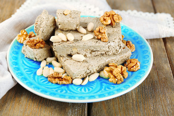 Sunflower halva with nuts on plate, on wooden background