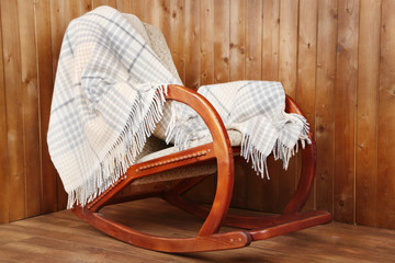 Fototapeta na wymiar Rocking chair covered with plaid on wooden wall background