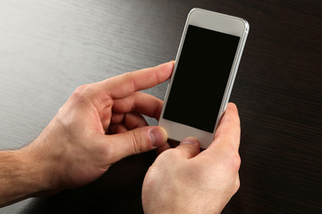 Hands holding smart mobile phone on wooden table background